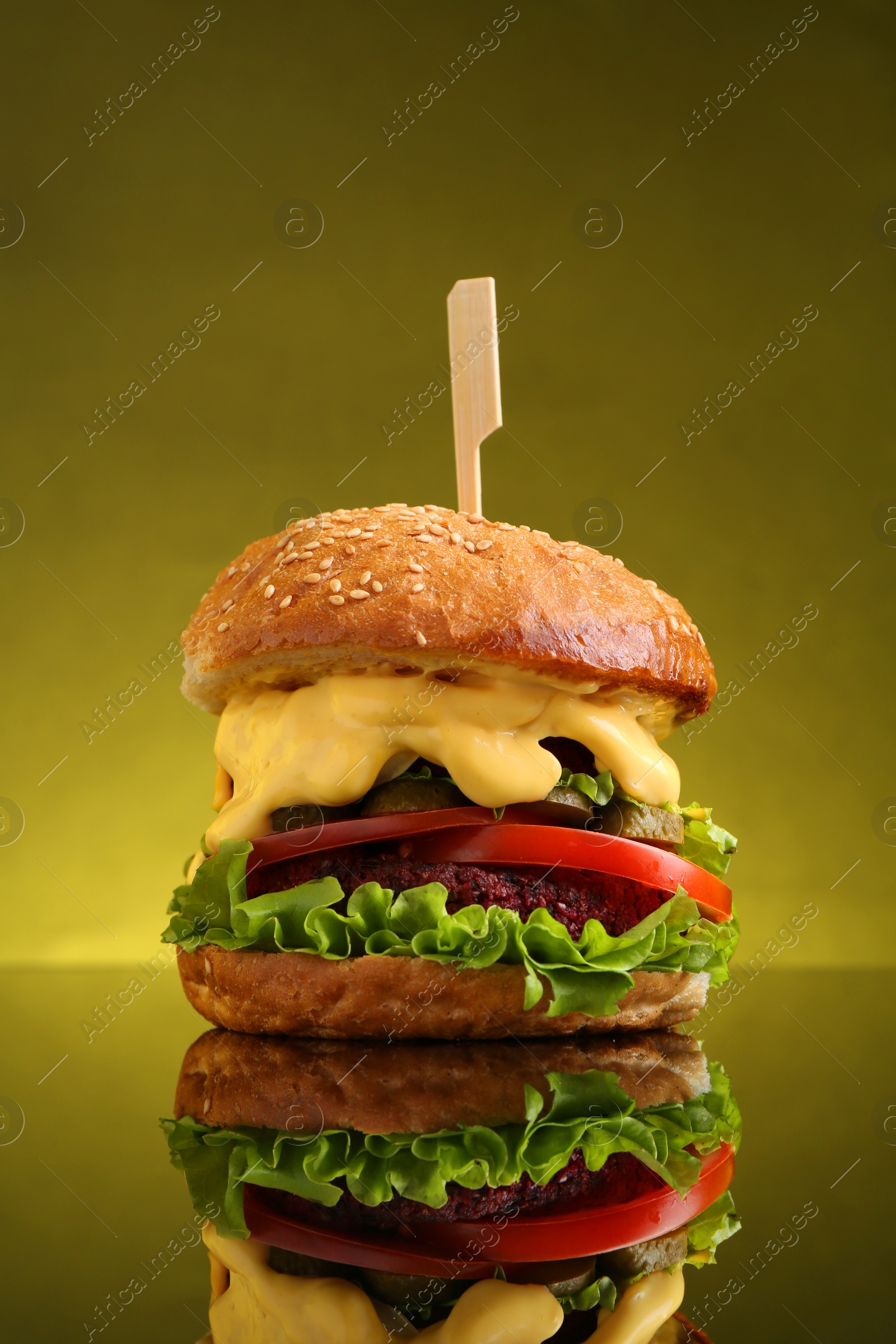 Photo of Delicious vegetarian burger on mirror surface against olive background