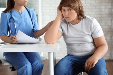 Photo of Emotional overweight boy consulting with doctor in clinic