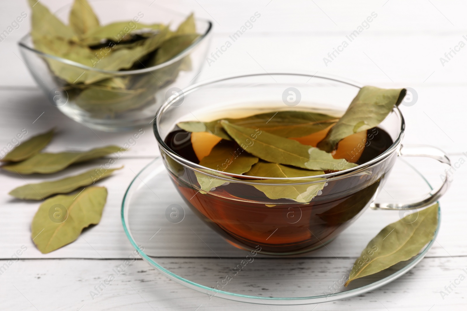 Photo of Cup of freshly brewed tea with bay leaves on white wooden table, closeup