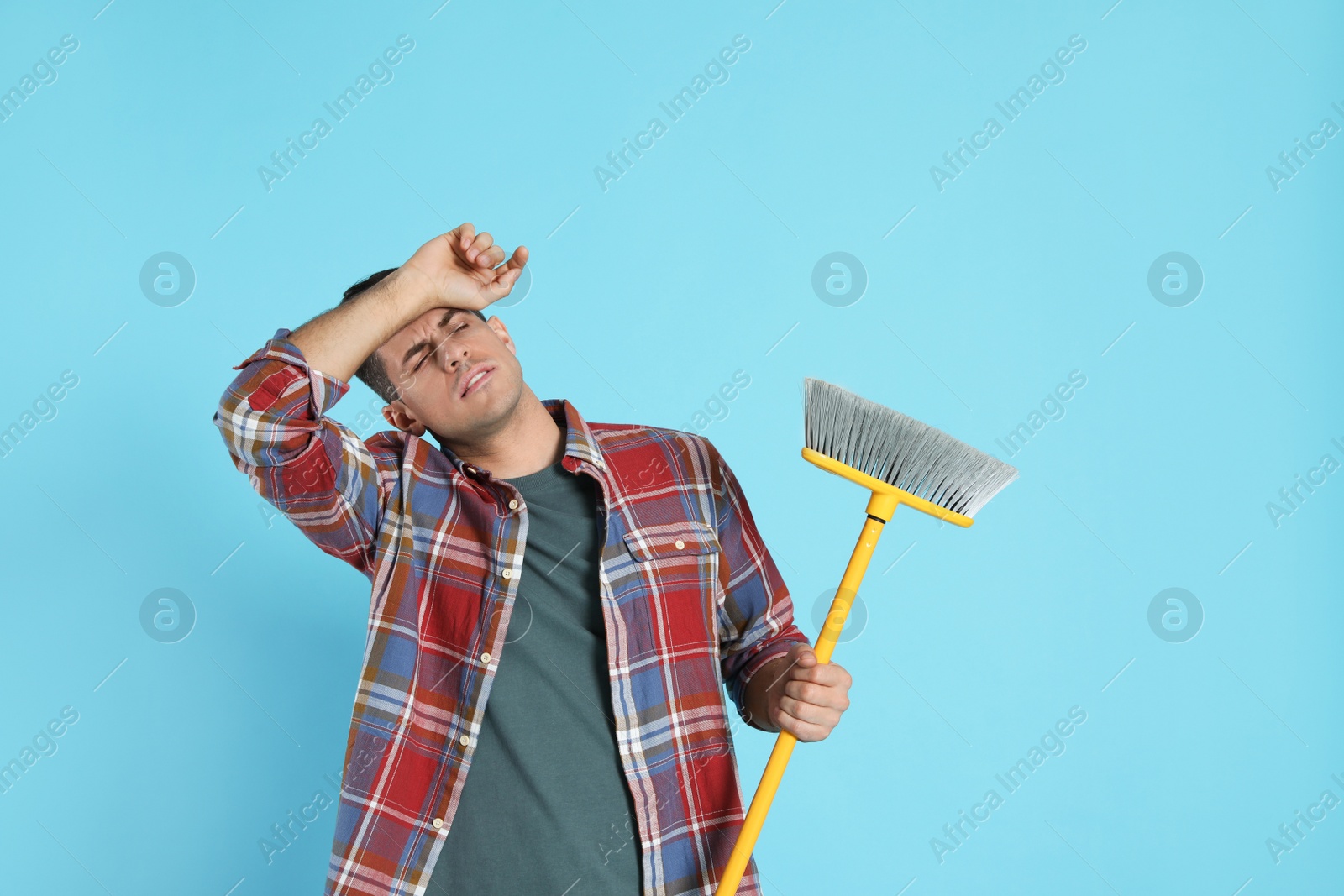 Photo of Tired man with yellow broom on light blue background