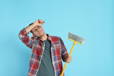 Tired man with yellow broom on light blue background