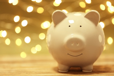 Photo of Cute piggy bank on table against blurred Christmas lights. Space for text