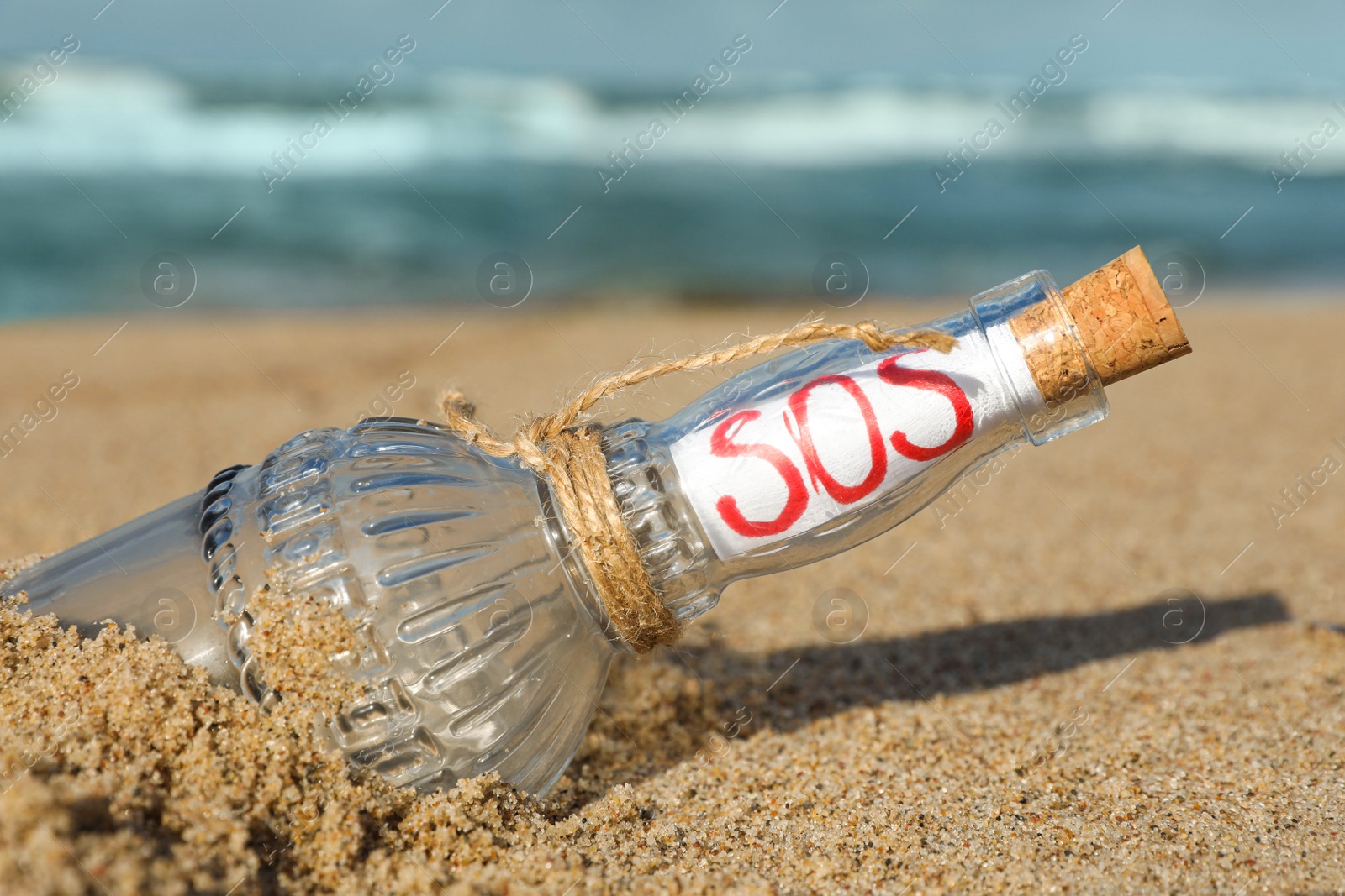 Photo of Glass bottle with SOS message on sand near sea, closeup