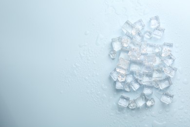 Photo of Crystal clear ice cubes on light blue background, flat lay. Space for text