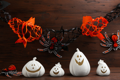 White pumpkin shaped candle holders and paper spider on wooden table. Halloween decoration