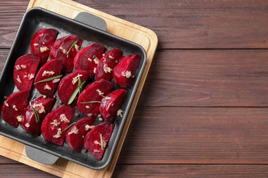 Photo of Baking dish with raw beetroot slices, garlic and rosemary on wooden table, top view. Space for text