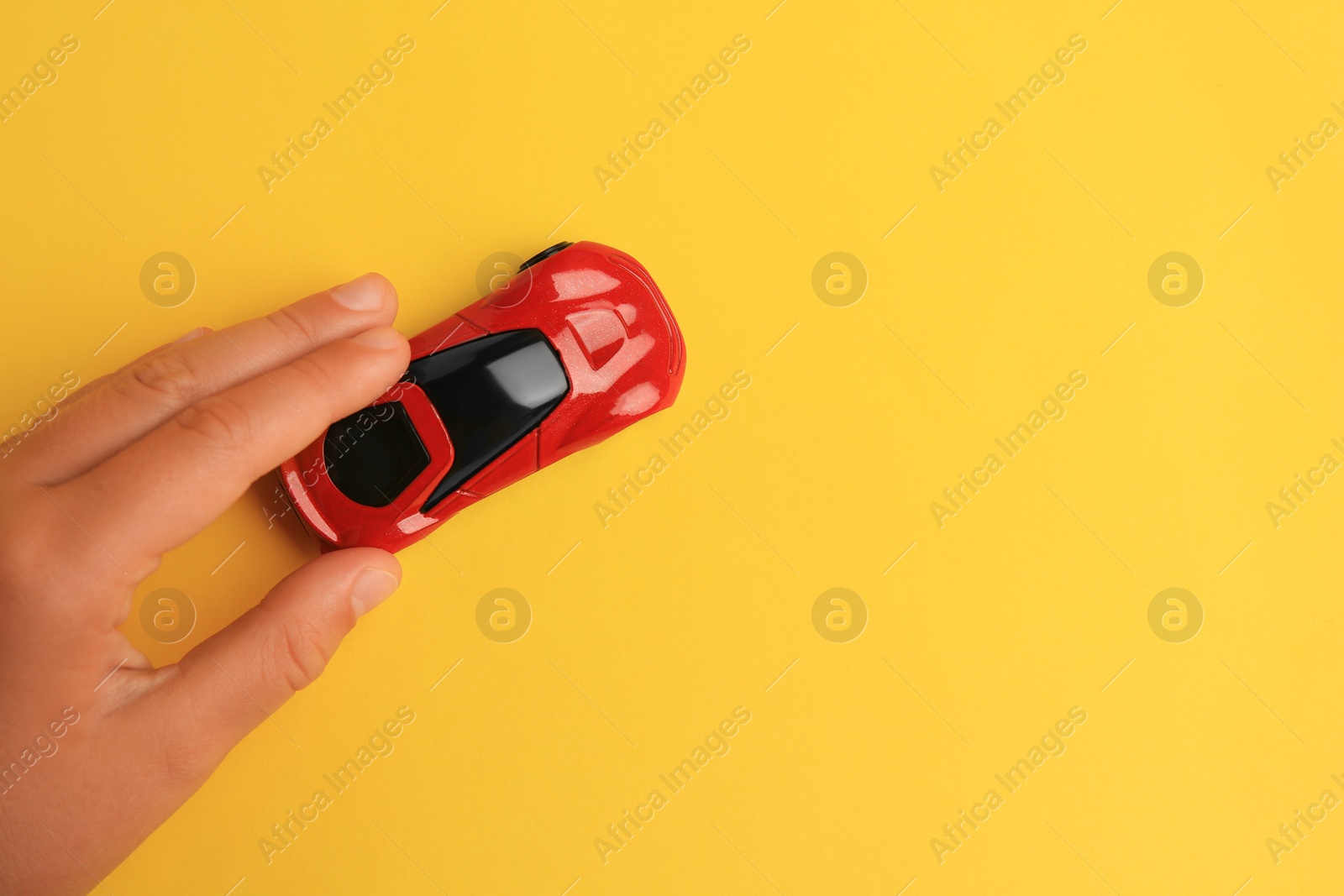 Photo of Child playing with toy car on yellow background, top view. Space for text