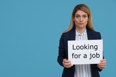 Unemployed woman holding sign with phrase Looking For A Job on light blue background. Space for text