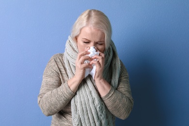 Mature woman with tissue suffering from cold on color background