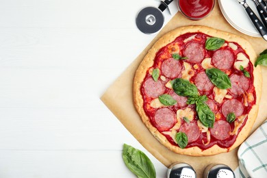 Pita pizza with pepperoni, cheese and basil on white wooden table, flat lay. Space for text