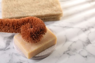 Photo of One cleaning brush and bar of soap on white marble table, closeup. Space for text