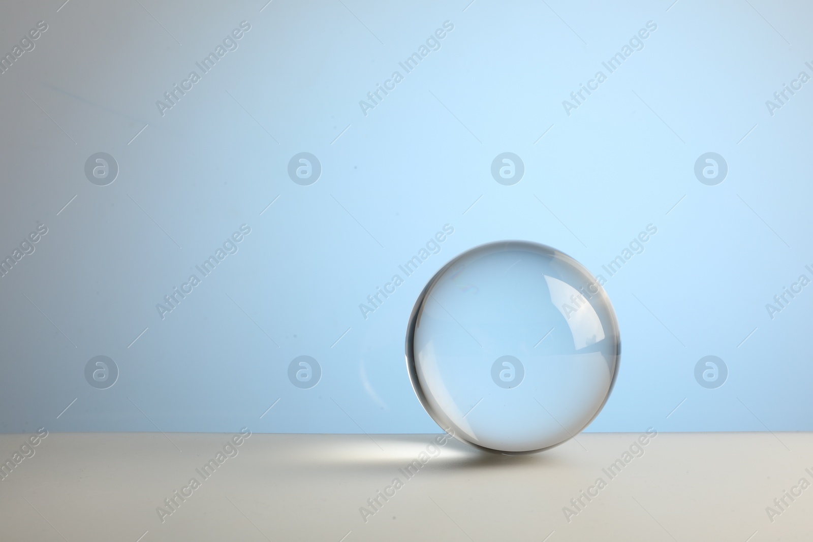 Photo of Transparent glass ball on table against light blue background. Space for text