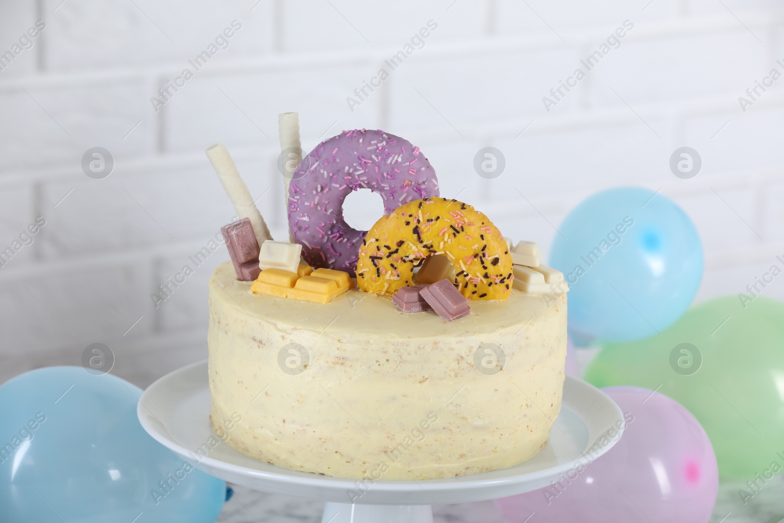 Photo of Delicious cake decorated with sweets and balloons against white brick wall