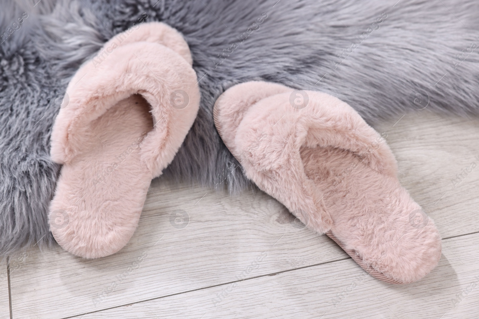 Photo of Pink soft slippers on light wooden floor at home, closeup