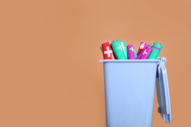 Photo of Many used batteries in recycling bin on light brown background. Space for text