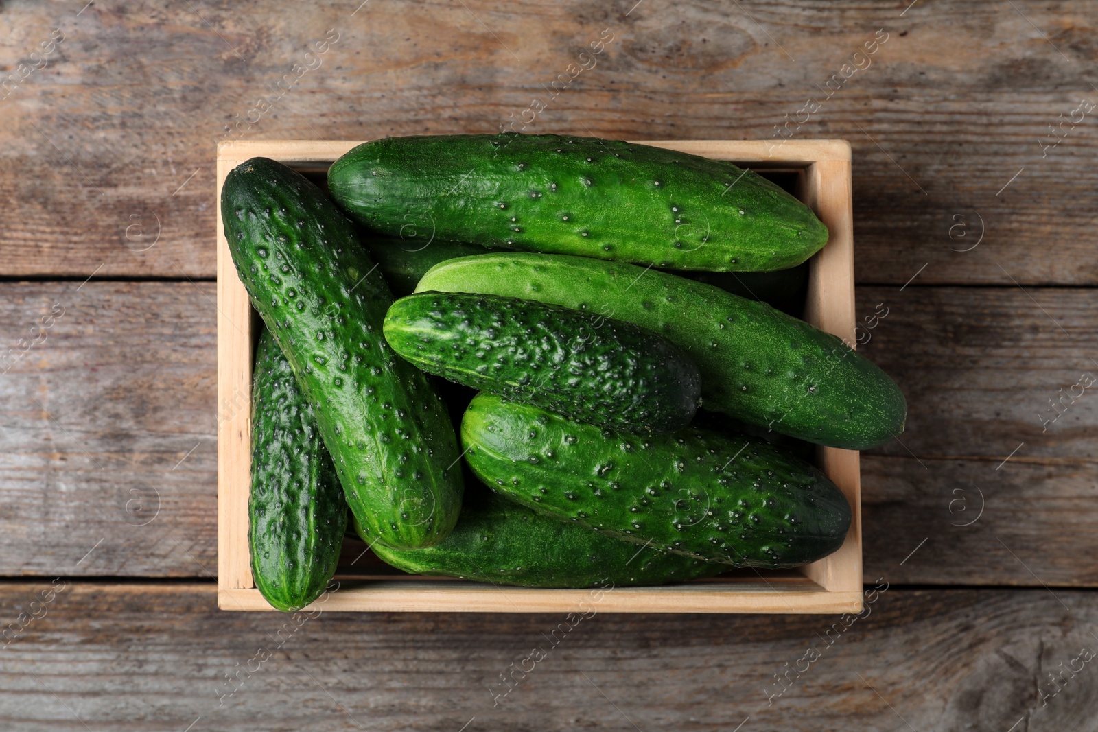 Photo of Crate full of fresh ripe cucumbers on wooden background, top view