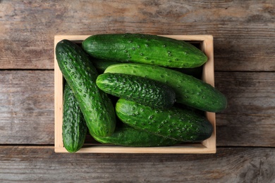 Photo of Crate full of fresh ripe cucumbers on wooden background, top view
