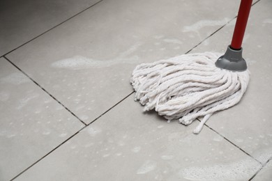 Cleaning grey tiled floor with string mop, space for text
