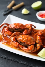 Photo of Delicious boiled crabs with sauce and lime on black textured table, closeup