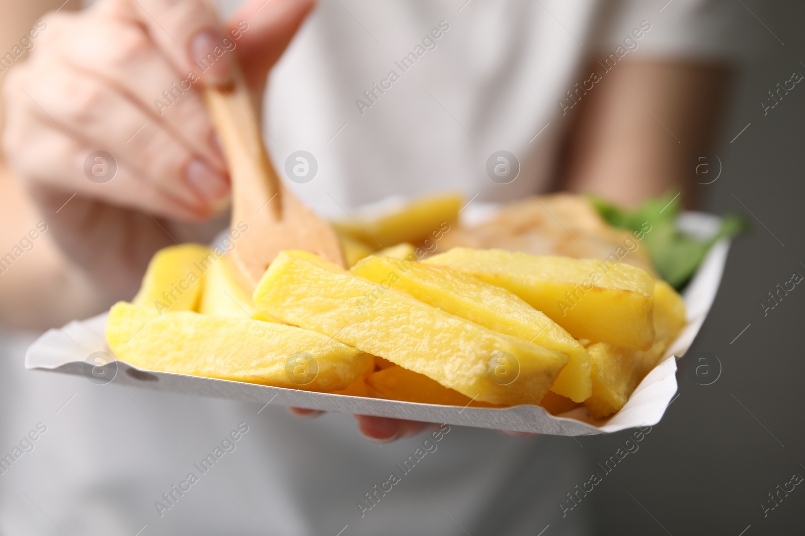 Photo of Woman eating delicious fish and chips on gray background, closeup