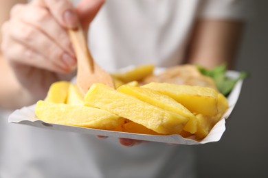 Photo of Woman eating delicious fish and chips on gray background, closeup