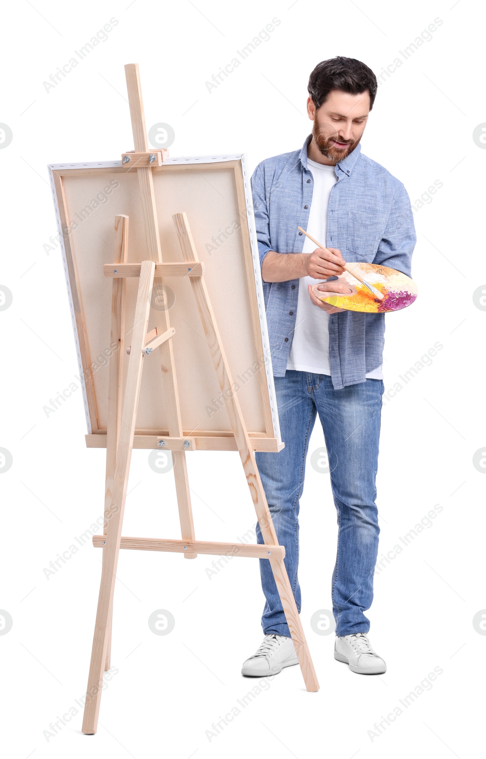 Photo of Man painting with brush against white background. Using easel to hold canvas