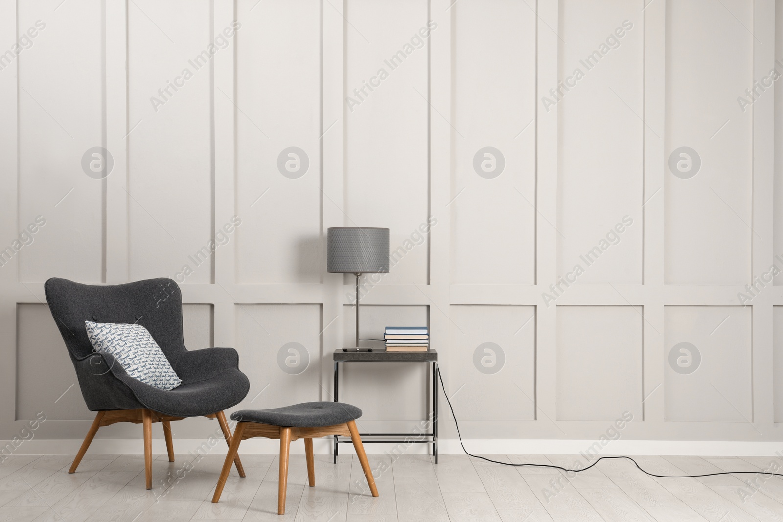 Photo of Comfortable armchair, table with lamp and books near light grey wall in room, space for text. Interior design