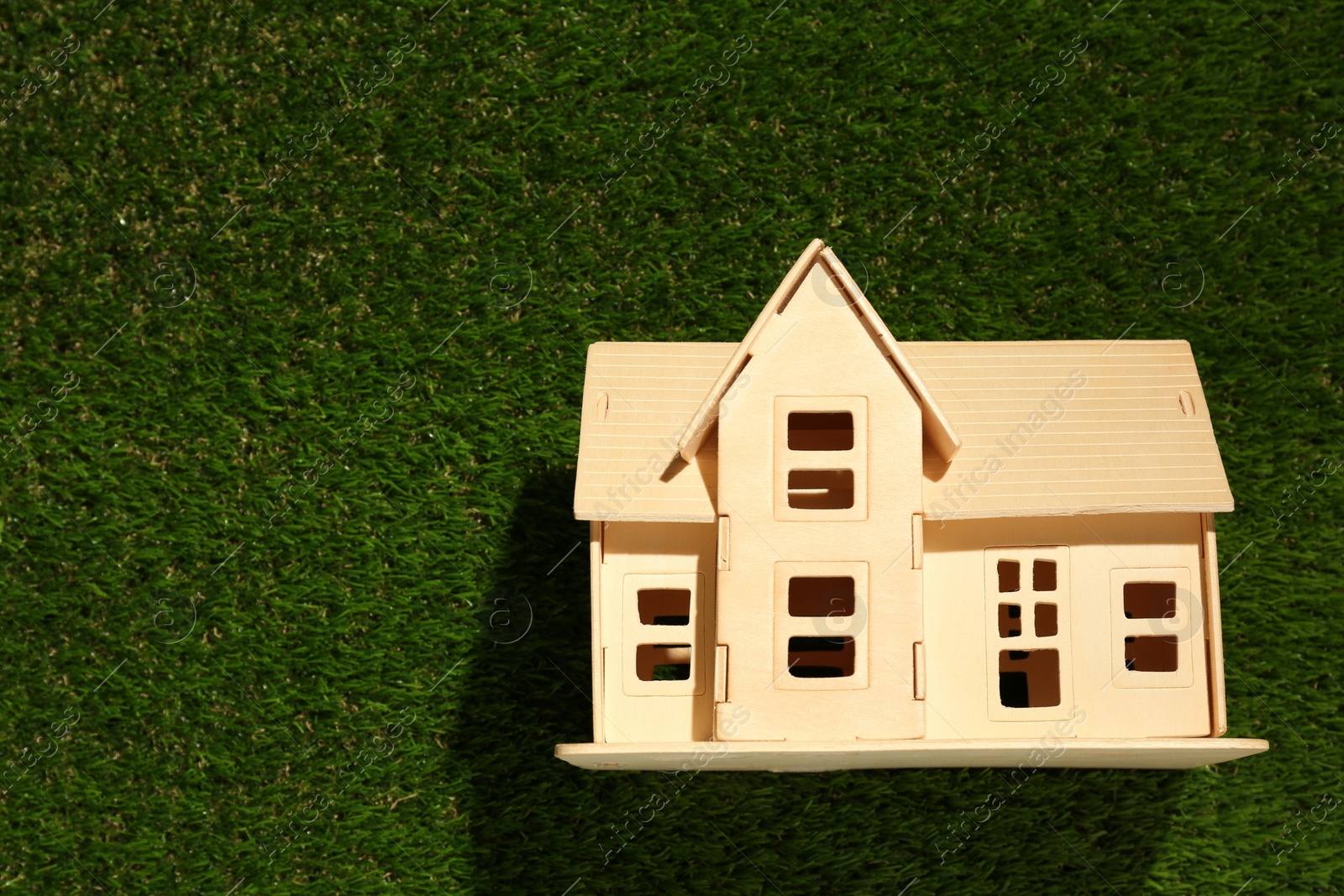 Photo of Wooden house model on green grass, top view. Space for text