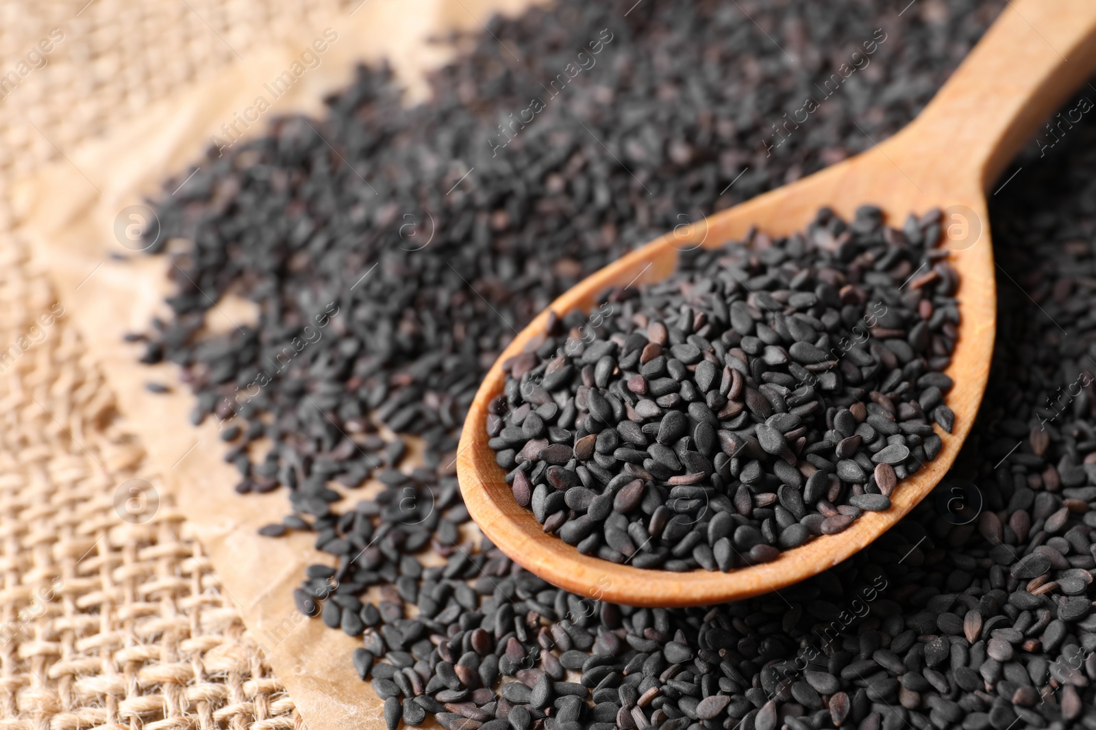 Photo of Black sesame seeds and wooden spoon on sack mat, closeup