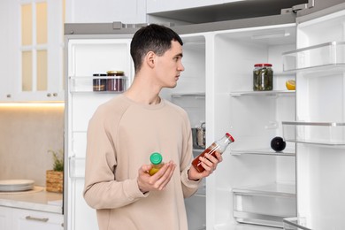 Upset man with sauces near empty refrigerator in kitchen