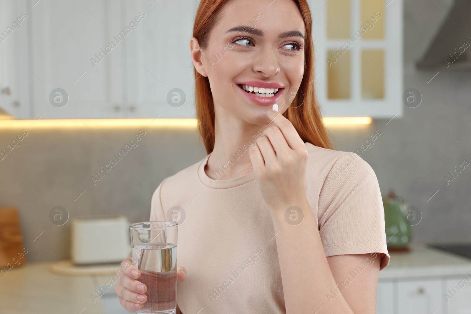 Photo of Beautiful young woman taking vitamin pill at home