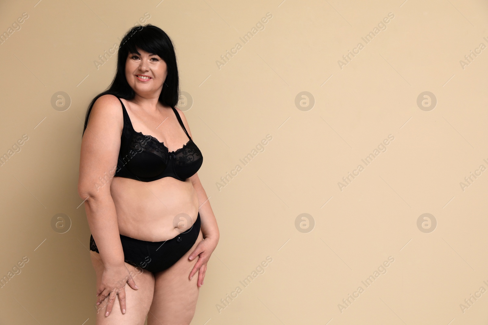 Photo of Beautiful overweight woman in black underwear on beige background, space for text. Plus-size model