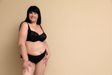 Beautiful overweight woman in black underwear on beige background, space for text. Plus-size model