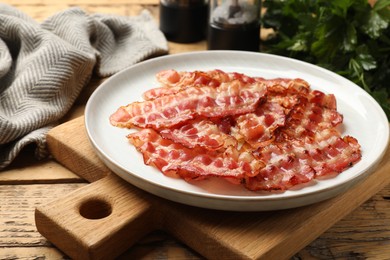 Photo of Plate with fried bacon slices on wooden table, closeup