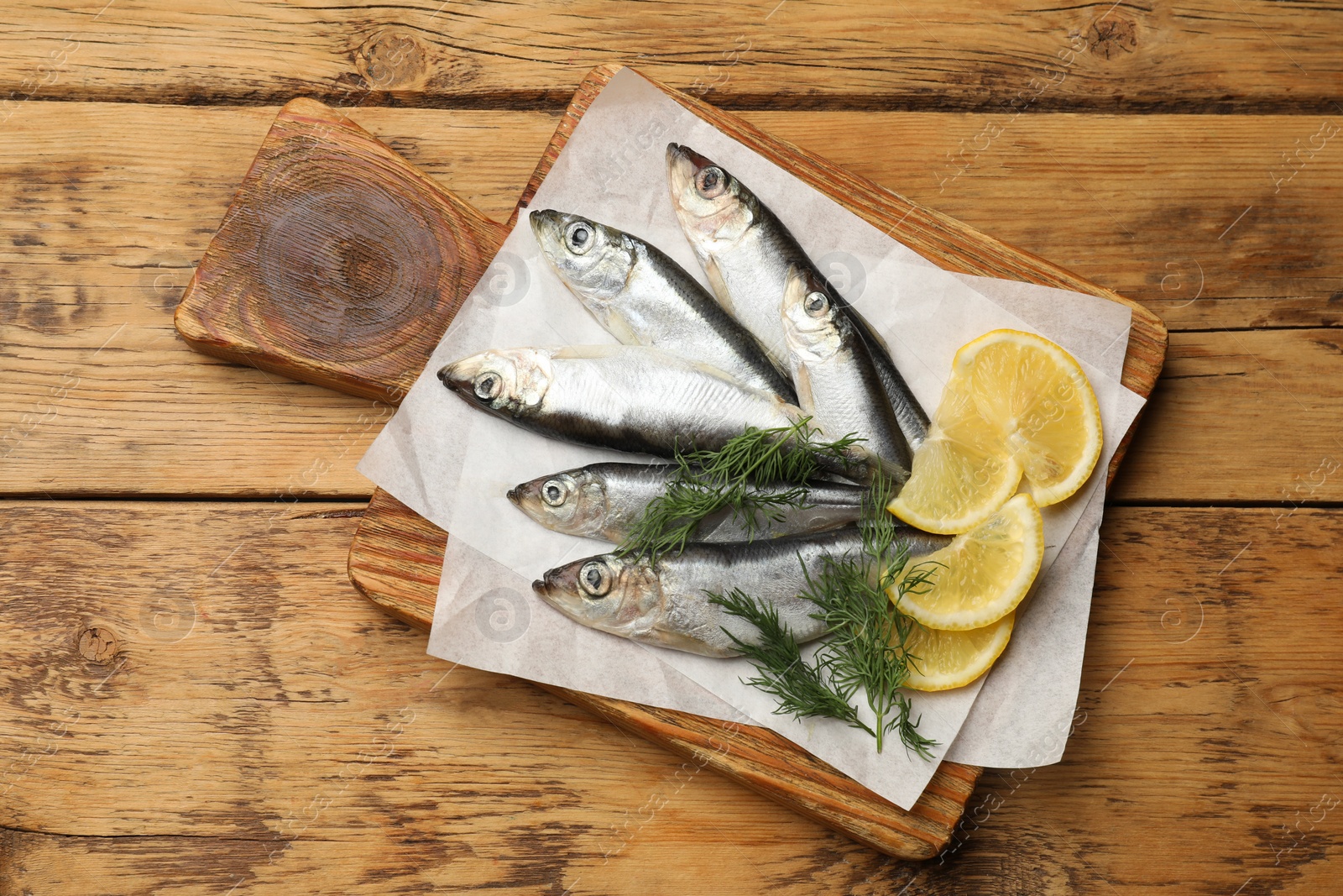 Photo of Fresh raw sprats, lemon and dill on wooden table, top view