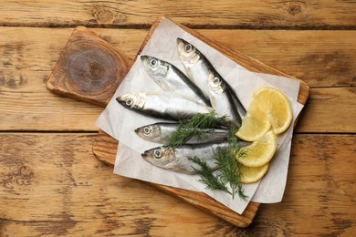 Fresh raw sprats, lemon and dill on wooden table, top view