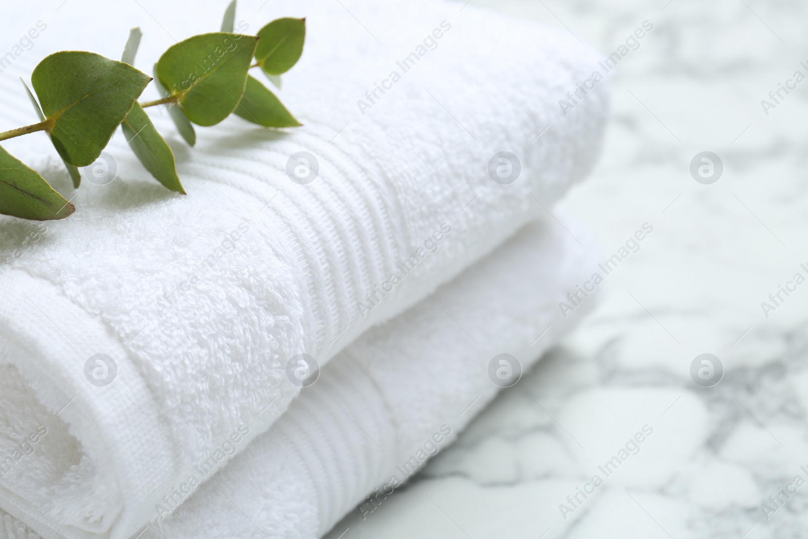 Photo of Folded terry towels and eucalyptus branch on white marble table, closeup