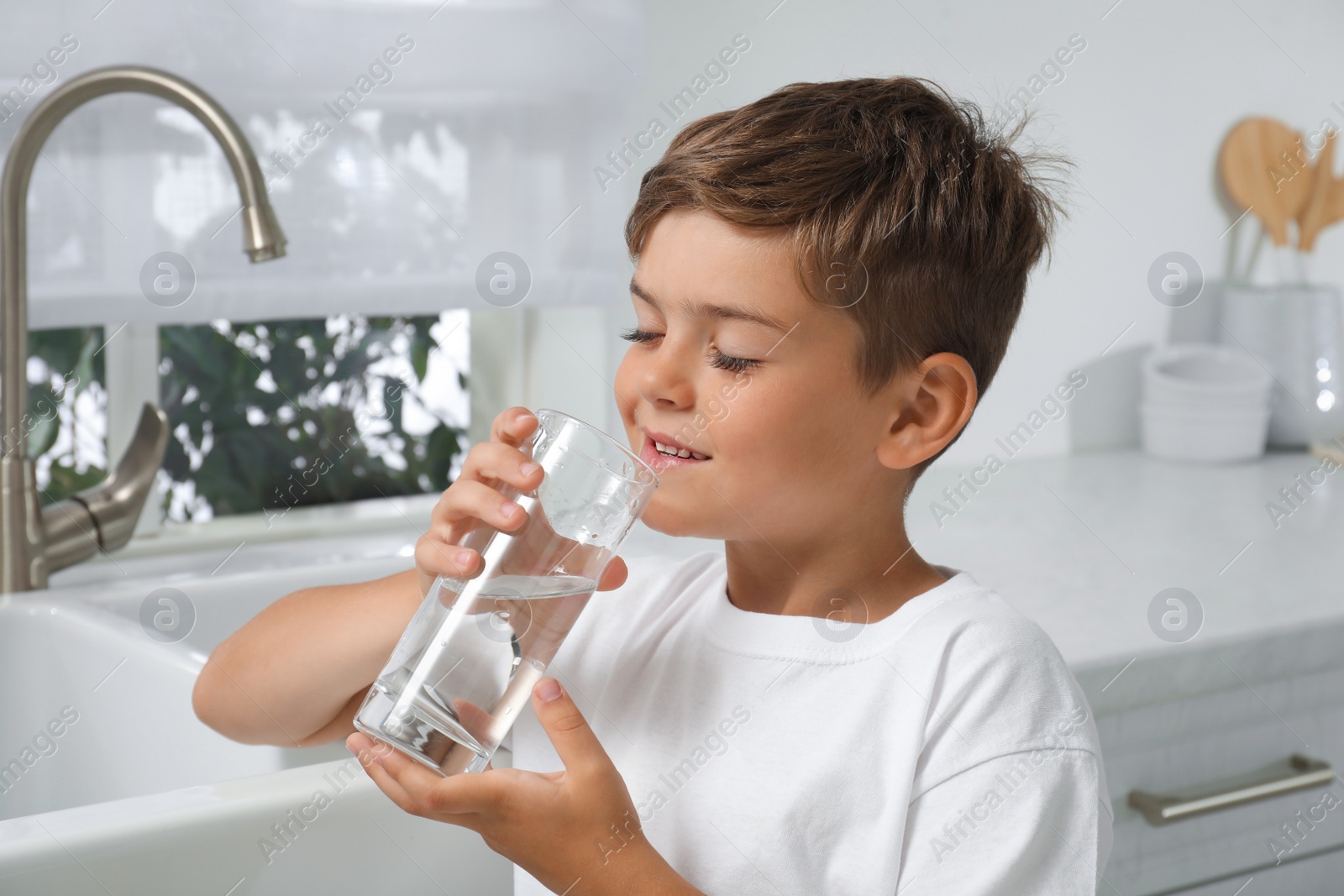 Photo of Boy drinking tap water from glass in kitchen