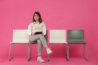 Young woman with tablet waiting for job interview on pink background