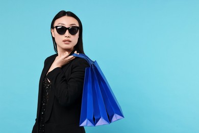 Beautiful woman with shopping bags on light blue background. Space for text