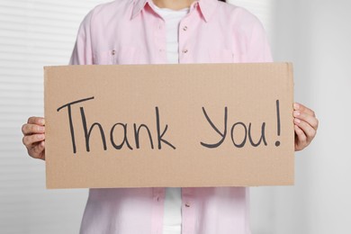 Photo of Woman holding cardboard sheet with phrase Thank You indoors, closeup