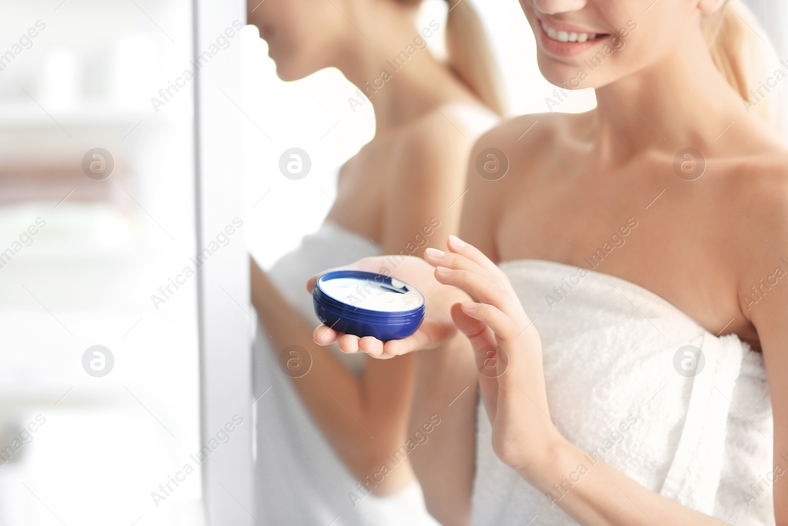 Photo of Young woman with jar of body cream at home