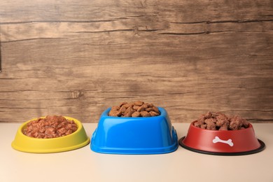 Photo of Dry and wet pet food in feeding bowls on beige background