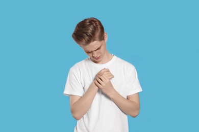 Photo of Teenage boy suffering from pain in hand on light blue background. Arthritis symptom