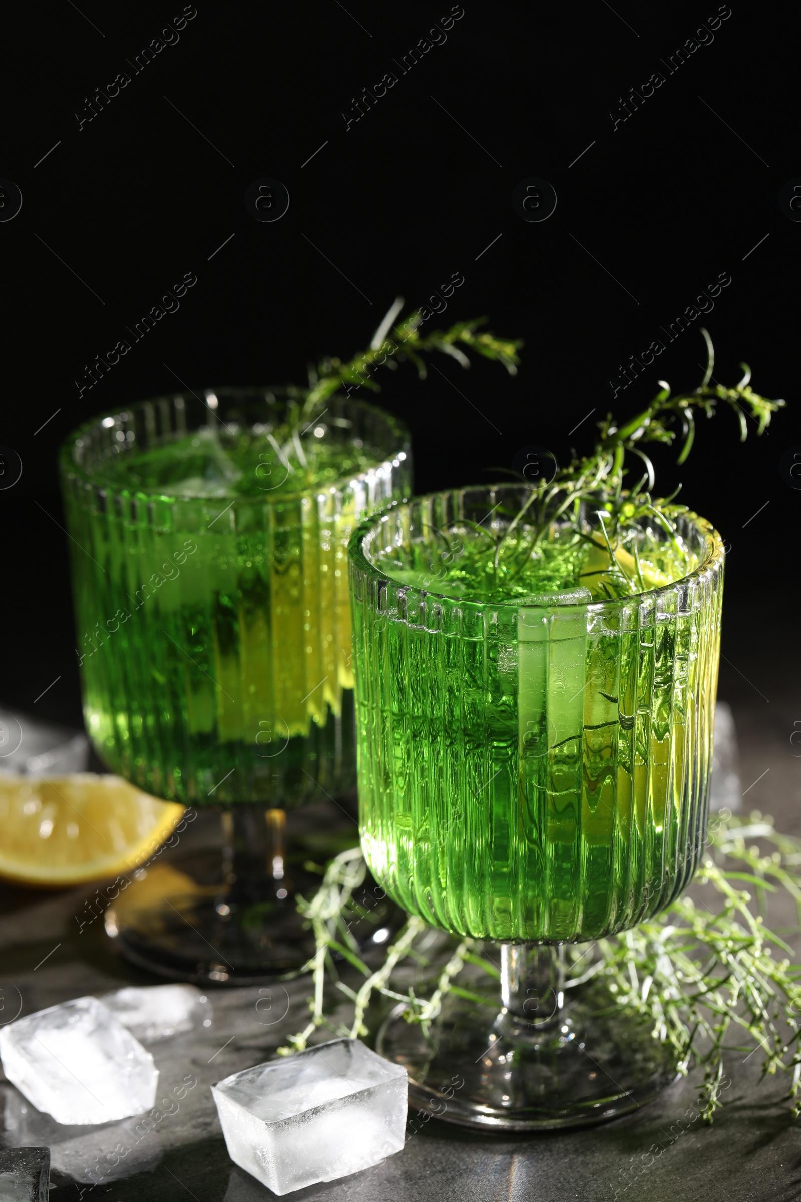 Photo of Glasses of homemade refreshing tarragon drink, ice cubes and sprigs on grey table