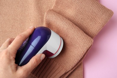 Photo of Woman using fabric shaver with sweater on pink background, top view. Space for text