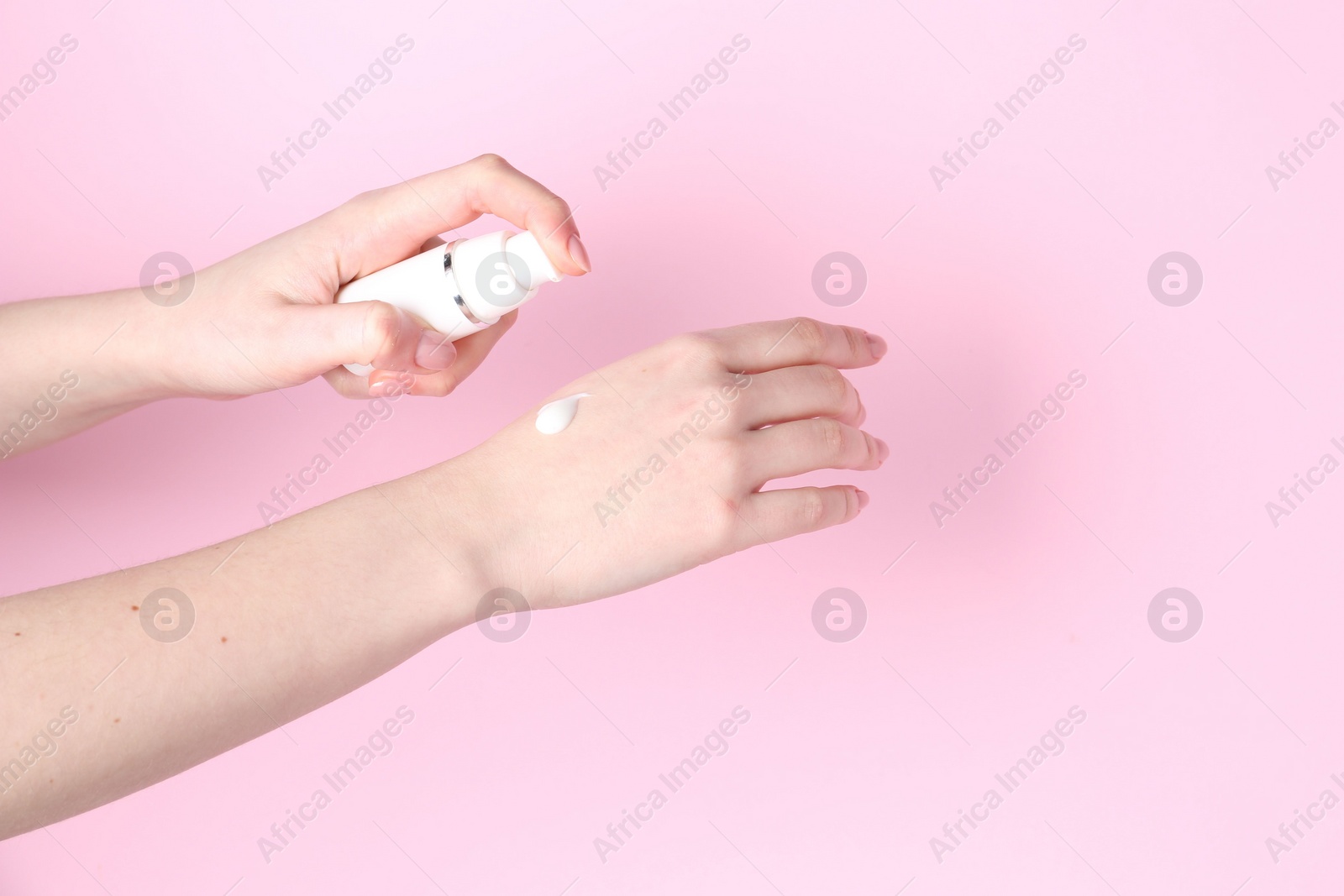 Photo of Woman applying cream on her hand against pink background, closeup. Space for text