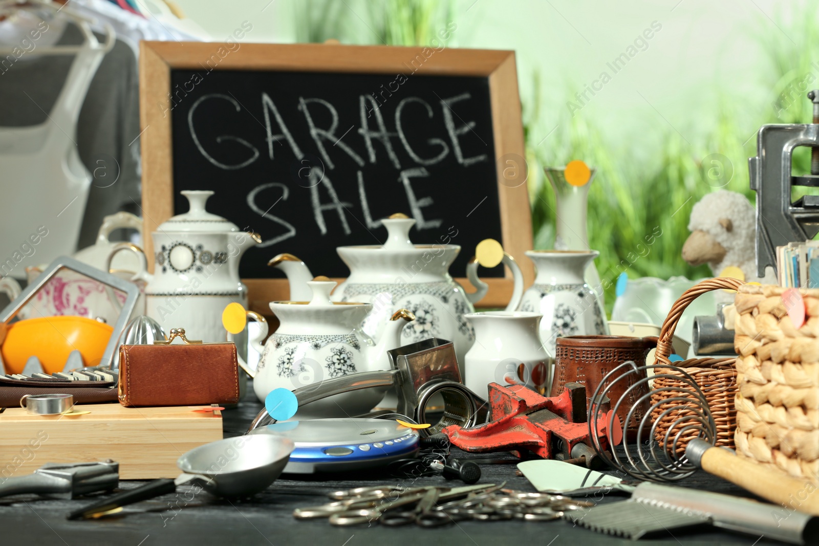 Photo of Blackboard with sign Garage Sale and many different stuff on black wooden table indoors