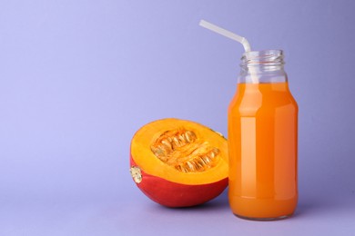 Tasty pumpkin juice in glass bottle and cut pumpkin on lavender color background, space for text