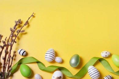 Photo of Flat lay composition with festively decorated Easter eggs and pussy willow branches on yellow background. Space for text
